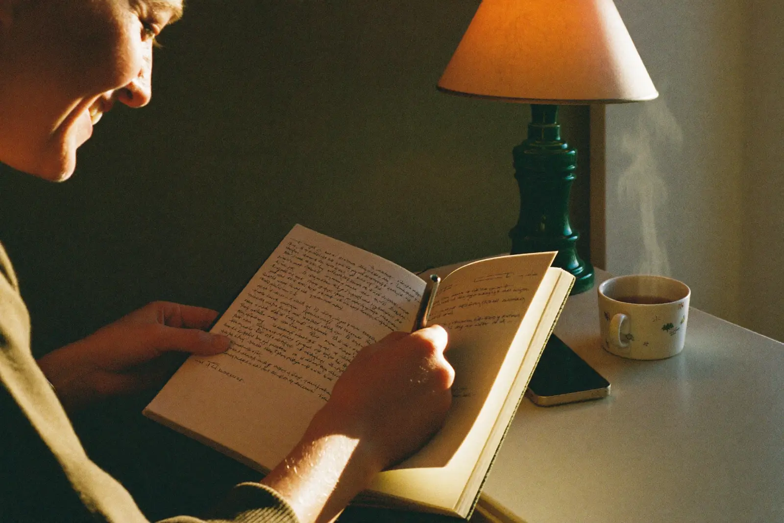 Person lächelt beim Journaling am Abend, Handy liegt umgedreht daneben
